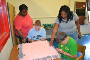 TWE employees work on making a fluffy pink and gray pet bed. 